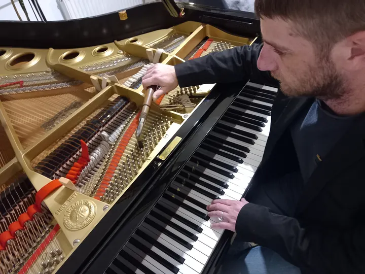 Simon Pacor accorde un piano droit, la main posée sur la mécanique