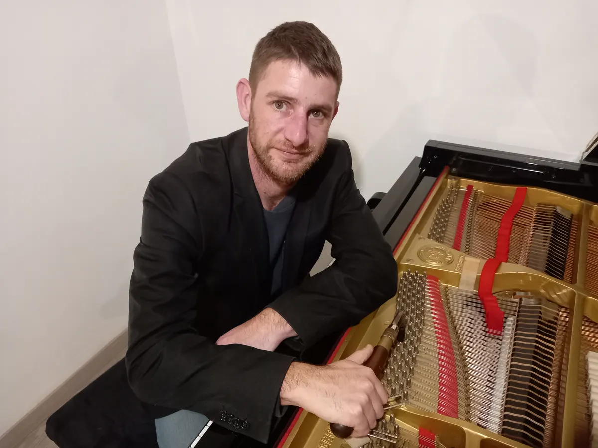Simon Pacor assis devant un piano droit ouvert, cordes et cadre visibles